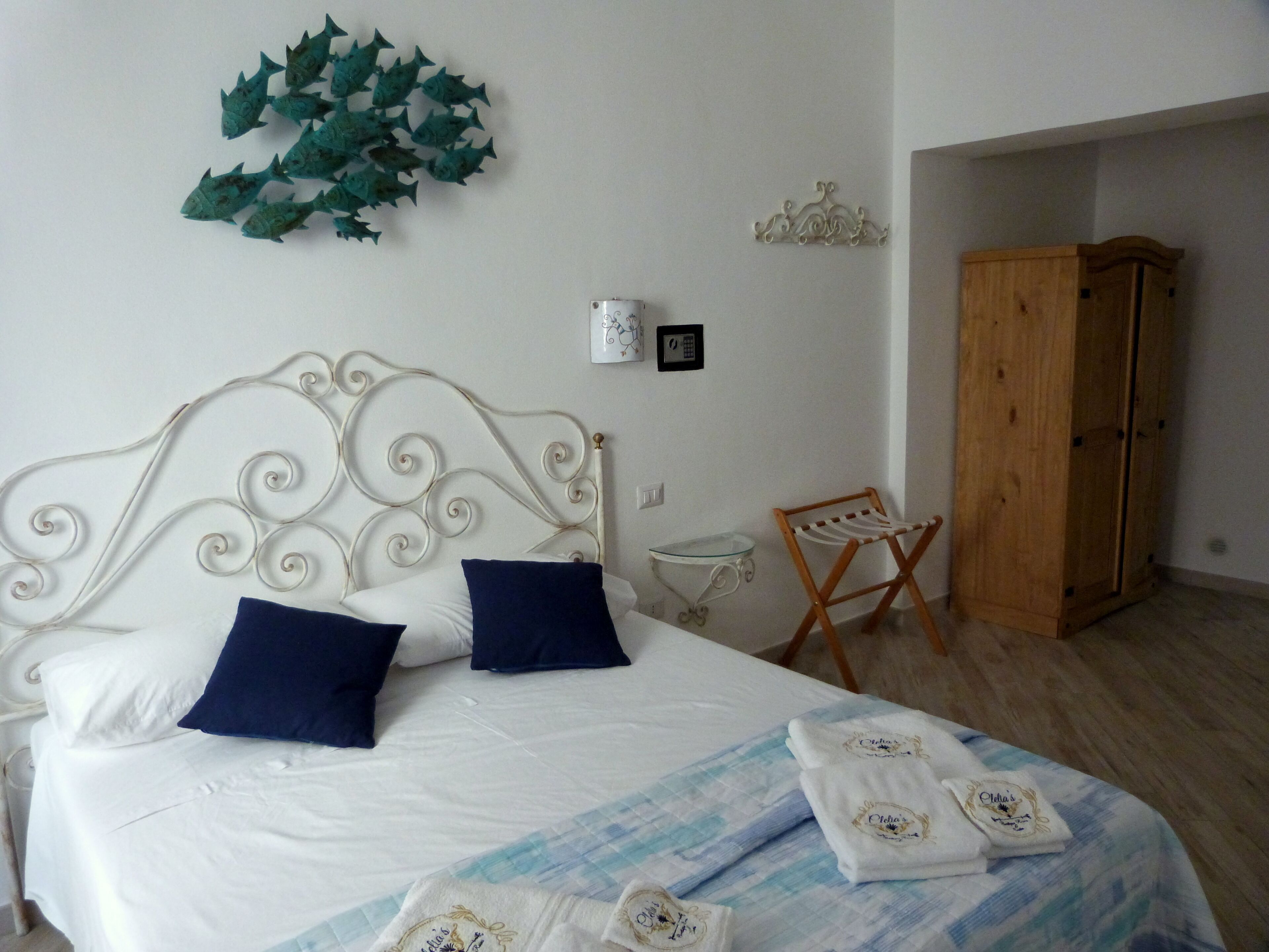 Un lit bien fait, avec une literie blanche et bleue, une décoration murale, une petite table et une armoire en bois.