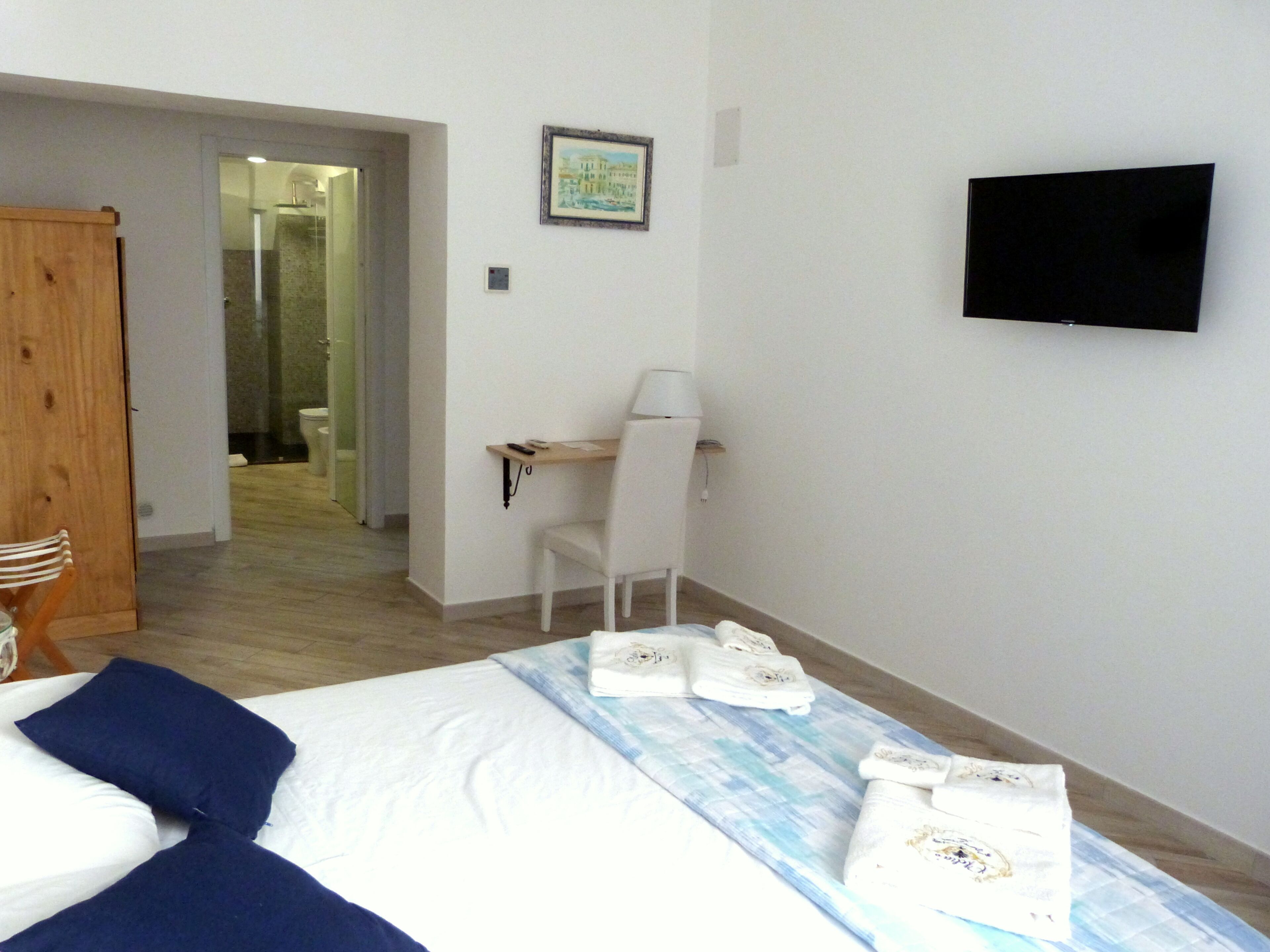 A hotel room with a bed, a desk, a chair, a TV, and a bathroom visible through an open door.