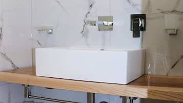 Un baño con lavamanos blanco, paredes de mármol y tocador de madera.