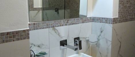 Baño con lavamanos blanco, espejo y ducha.