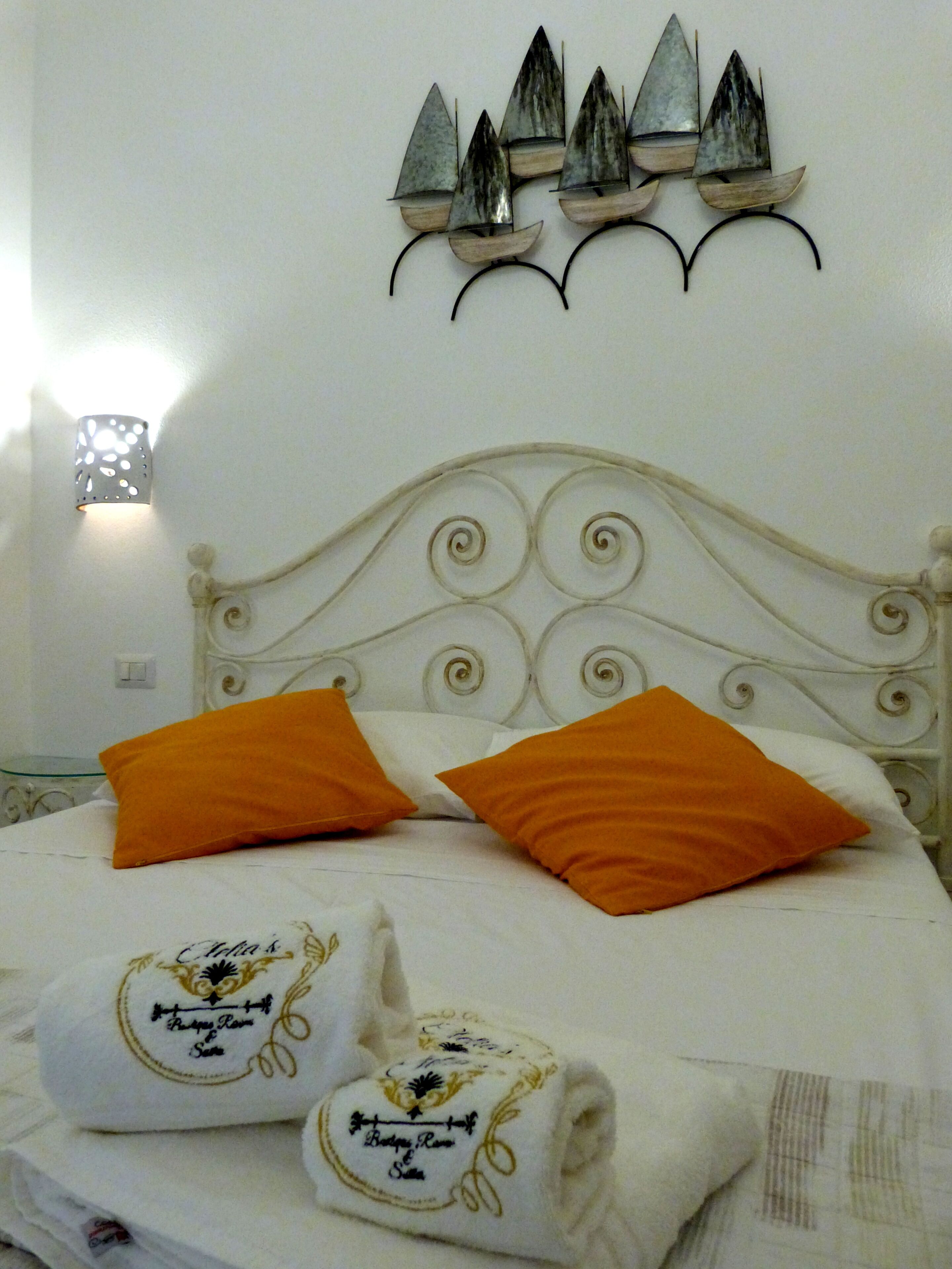 A bed with two orange pillows, a white headboard, and a wall-mounted decorative piece above.