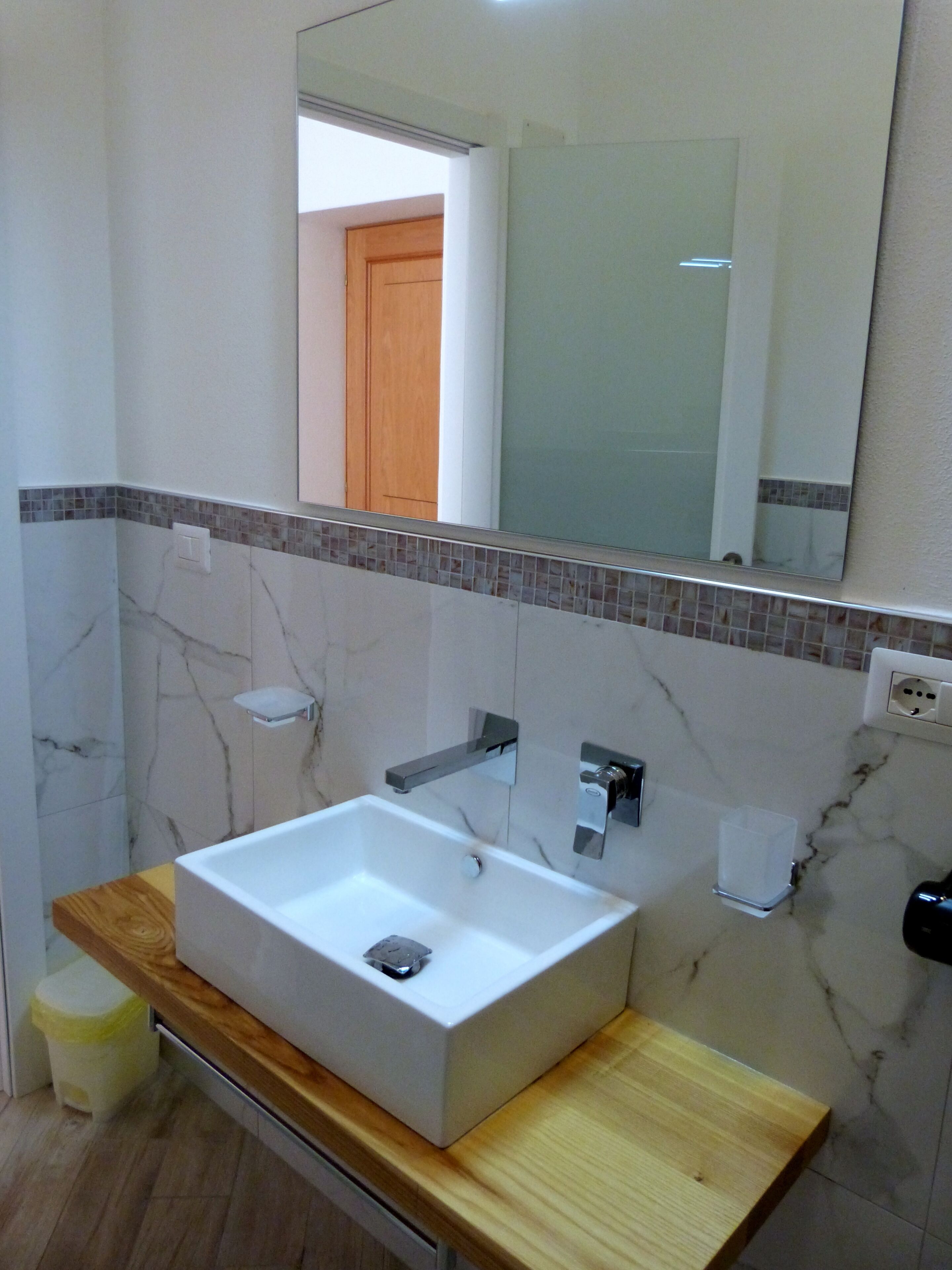 Un baño con un lavabo blanco, encimera de madera y un espejo encima.