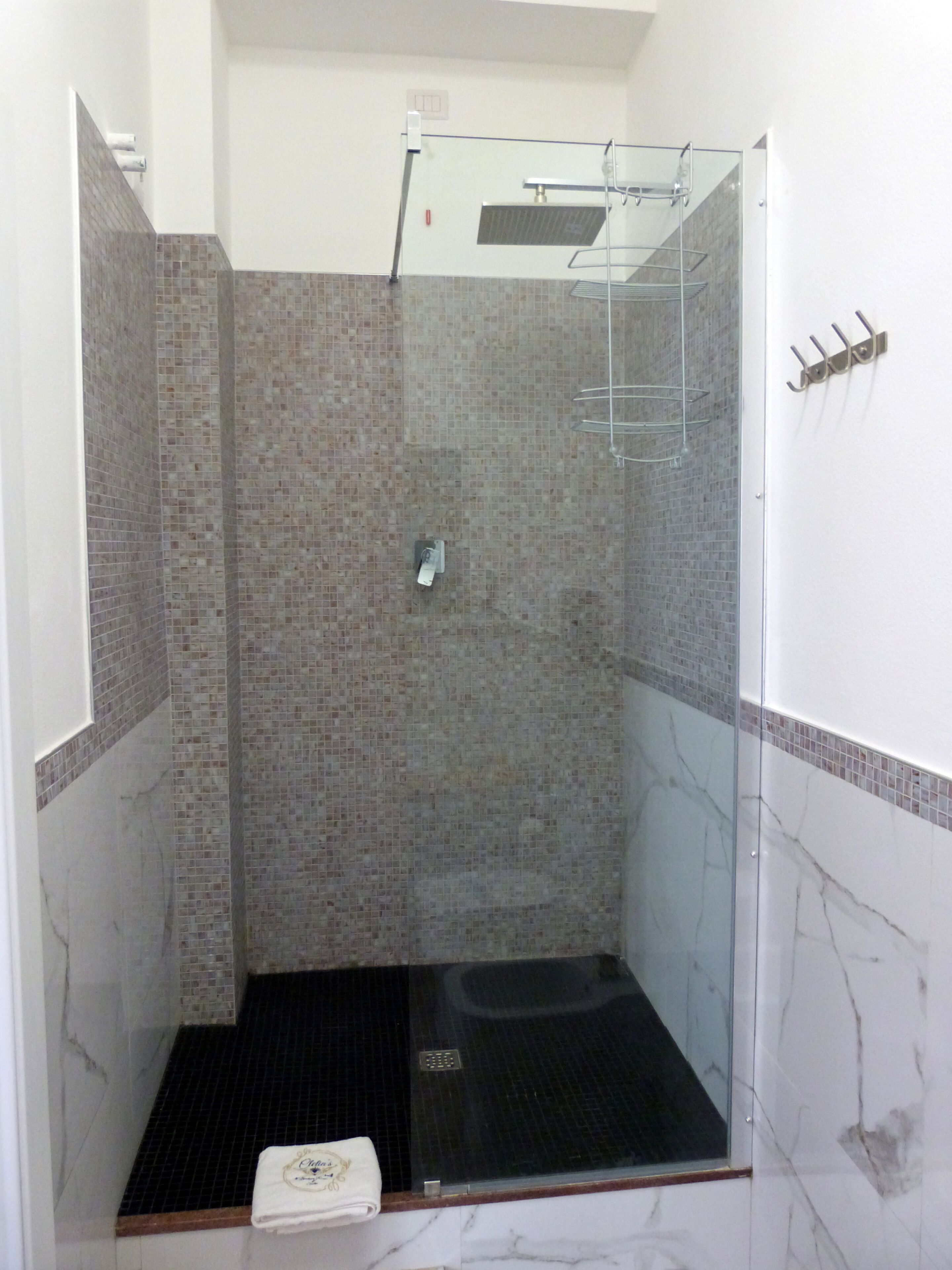 A glass-enclosed shower stall with a black floor, tiled walls, and a marble accent wall.
