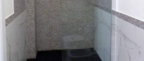 A glass-enclosed shower stall with a black floor, tiled walls, and a marble accent wall.