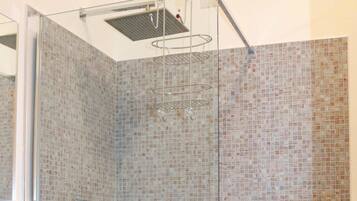 A modern bathroom with a glass shower enclosure, a marble sink, and mosaic tile walls.