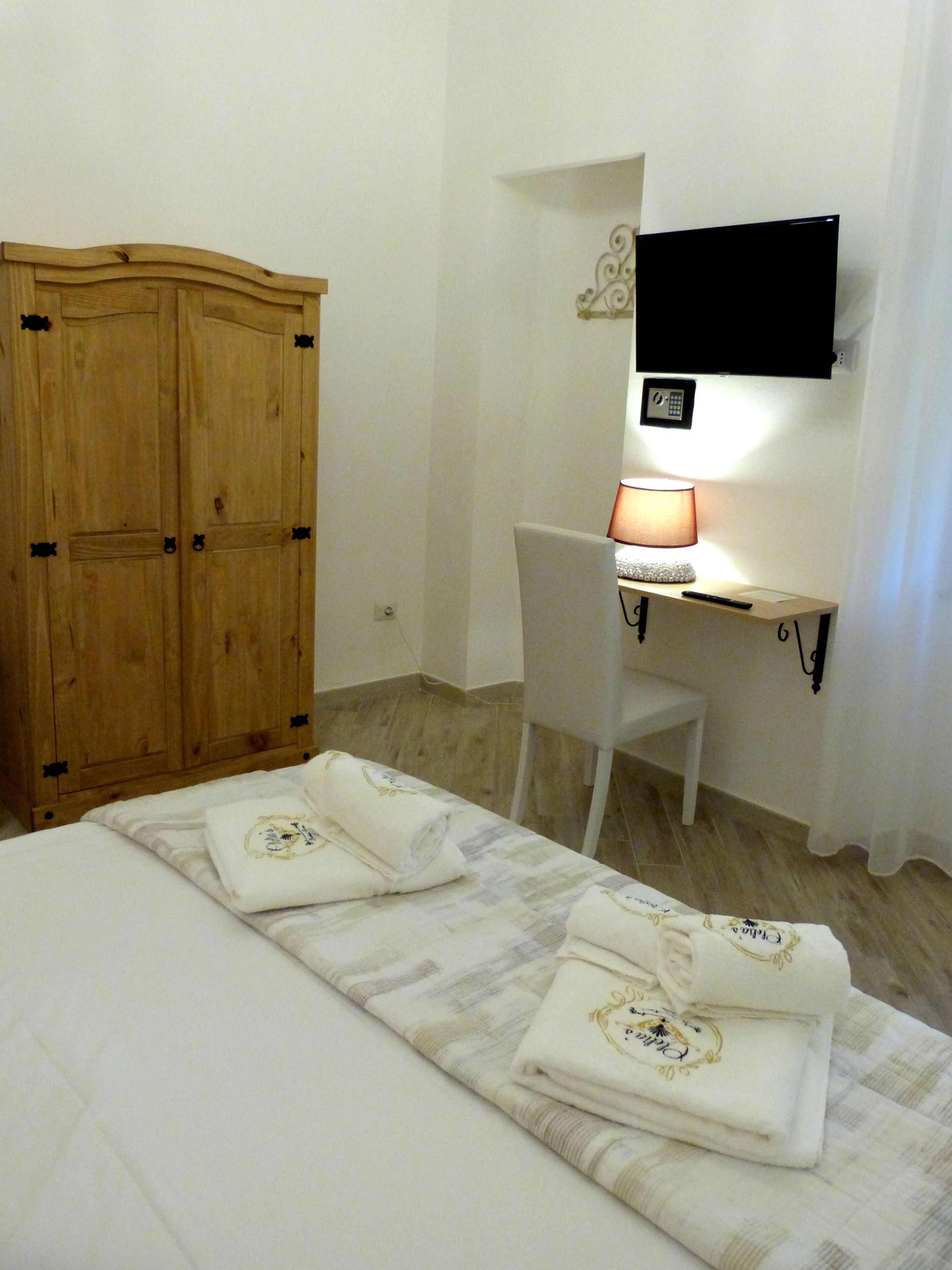 Una habitación de hotel con un armario de madera, un escritorio con lámpara y una cama con toallas.