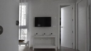 Ein minimalistisch eingerichteter Raum mit Wand-Fernseher, einem weißen Konsolentisch und einer Tür zu einem weiteren Zimmer.