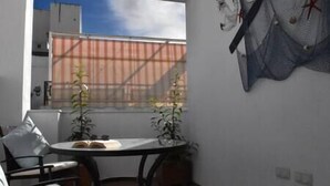 Ein kleiner, sonnendurchfluteter Raum mit Tisch und Stühlen, einem Fenster mit Blick auf ein Gebäude und einem Wandnetz.