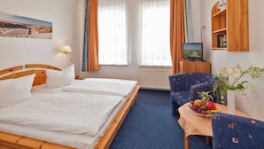Habitación de hotel con cama de madera, una mesita con fruta, un sofá, un televisor y una estantería con libros.