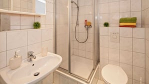 Un baño con ducha de vidrio, lavamanos con espejo e inodoro.