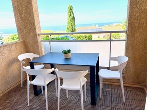 A balcony with a table and chairs, a potted plant, and a view of the sea and buildings. - Apartment for 4 people, 2 bedrooms, with a terrace and ocean view, air conditioning, private parking (MONTICELLO)