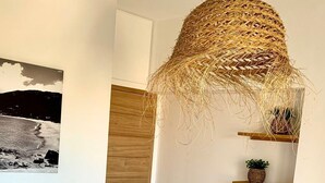 Ein schlicht eingerichtetes Schlafzimmer mit einem Bett, einer hängenden gewebten Leuchte, einer Holztür und einem Wandregal mit Pflanzen.
