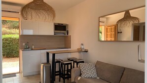 Eine moderne Küche mit weißen Schränken, einer Holz Arbeitsplatte und einer eingebauten Mikrowelle. Zwei schwarze Hocker und ein braunes Sofa mit einem gemusterten Kissen sind vorhanden. Ein großer Spiegel an der Wand spiegelt die Küche und eine Holztür wider.