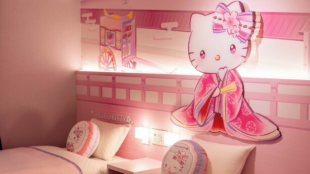Een kamer in roze tinten, met een Hello Kitty decoratie aan de muur en passend kussen op het bed.
