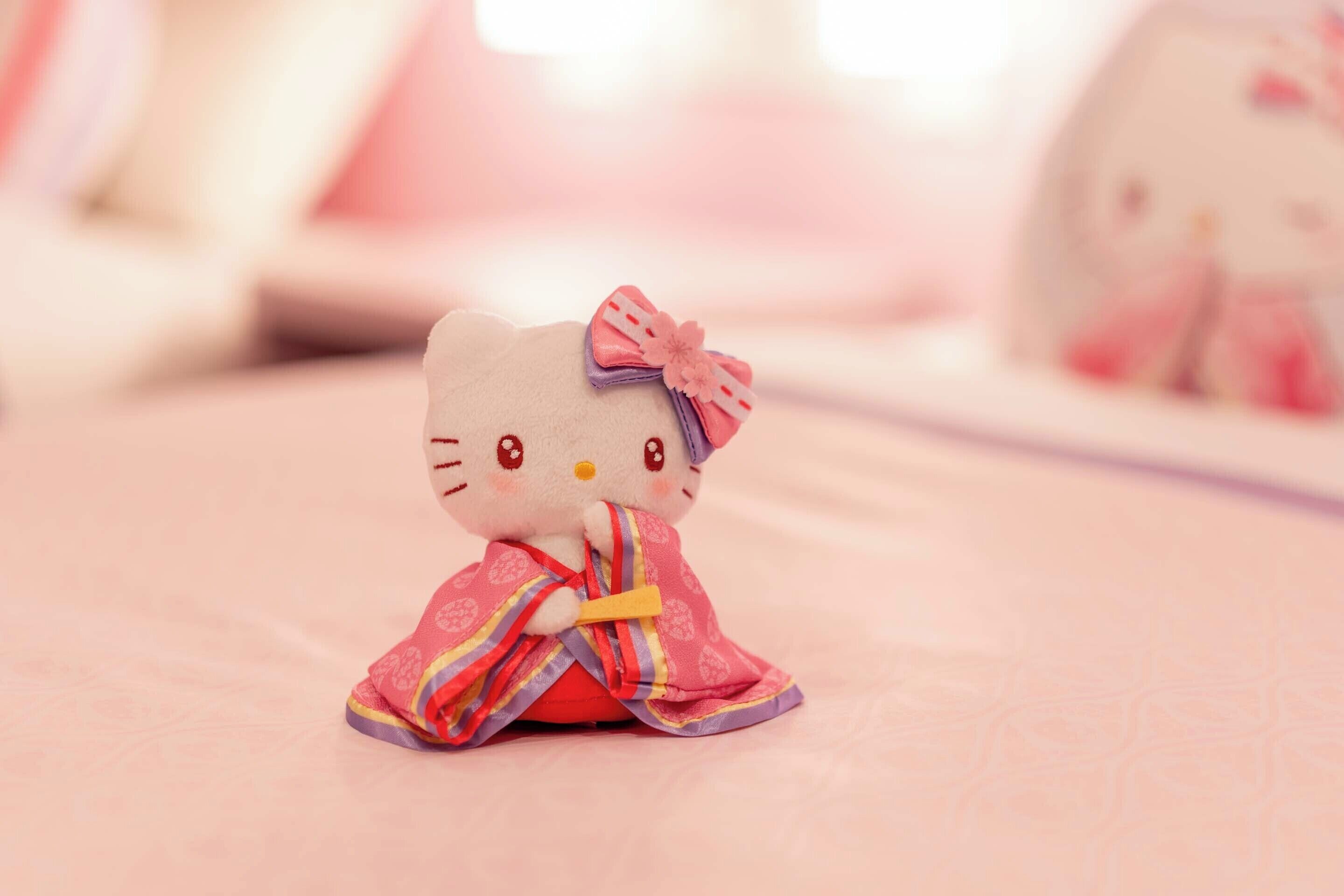 A Hello Kitty plush toy on a bed with a pink blanket.