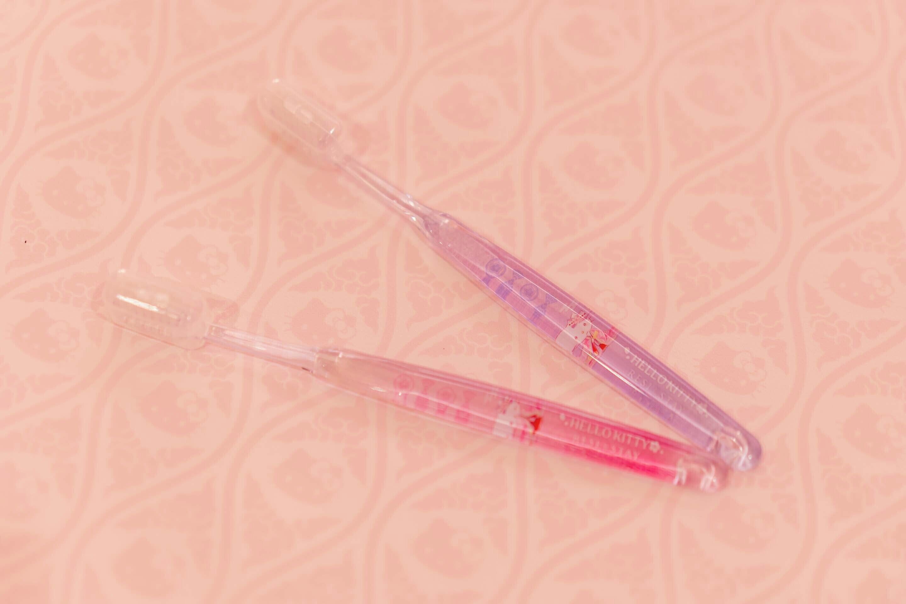 Two transparent thermometers with measurement markings on a patterned pink background.