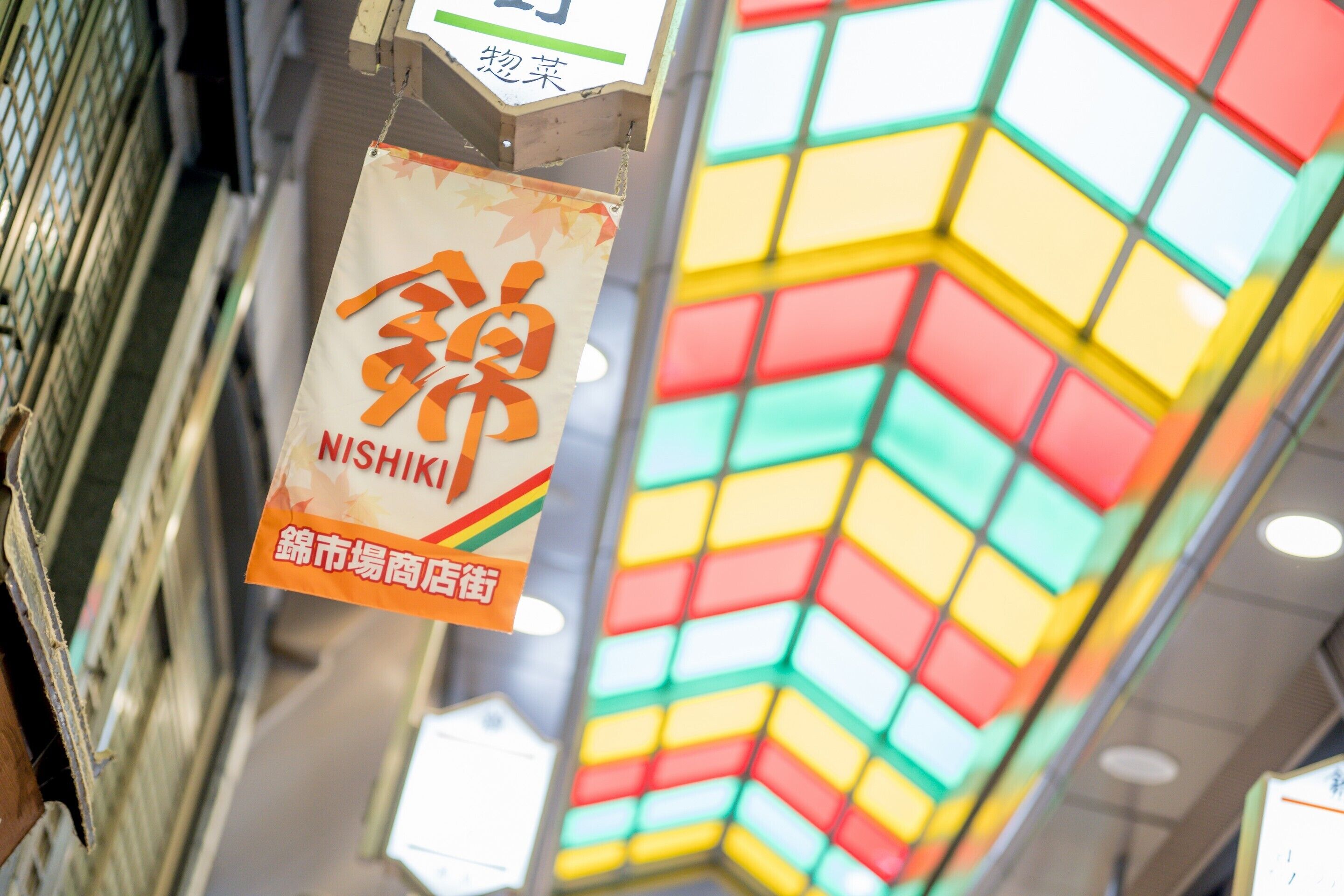 A colorful, geometric ceiling design with a hanging sign that reads "NISHIKI" and "NISHIKI MARKET SHOPPING STREET".