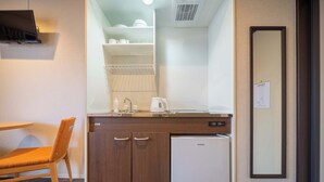 Een compacte hotelkamer met een houten stoel, een kleine kitchenette met een koelkast, een wastafel en een spiegel.