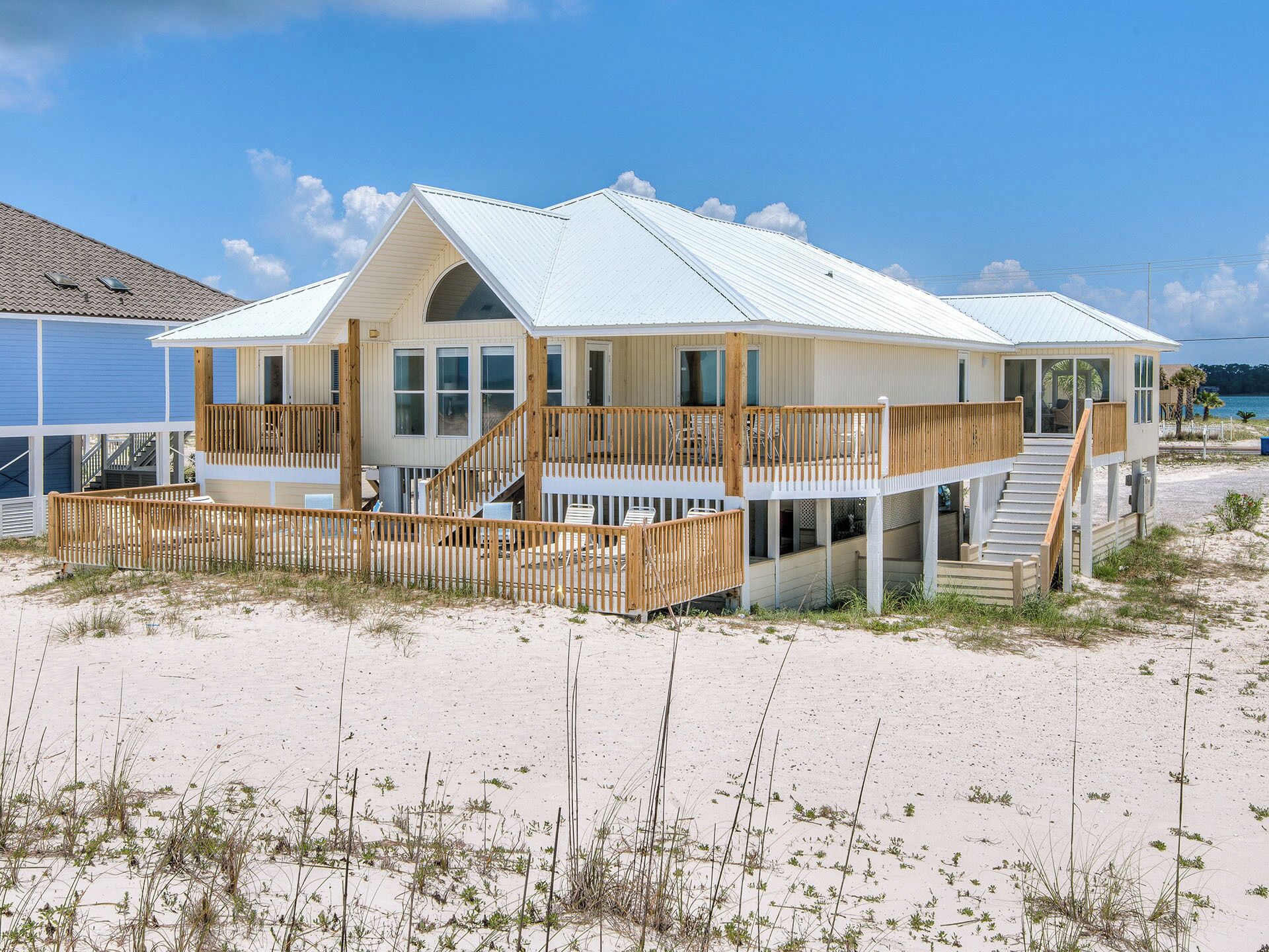 Een strandhuis met een houten terras, meerdere balkons en een overdekte veranda.