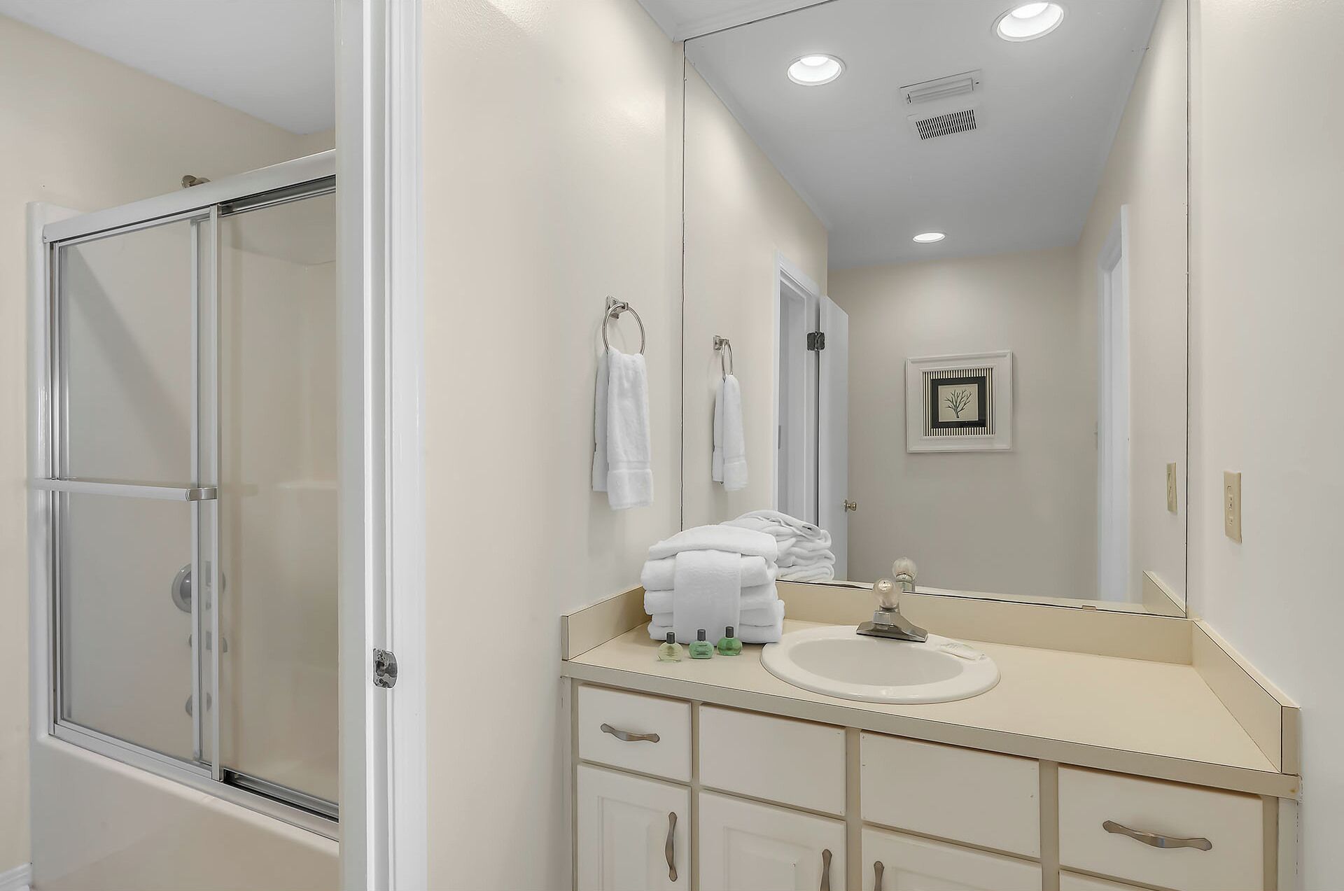 A bathroom with a glass shower door, a sink with a mirror, and a towel rack with folded towels.