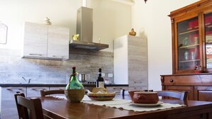 Een houten eettafel met stoelen, een keuken met kastjes, een fornuis en een kast met glazen deuren.