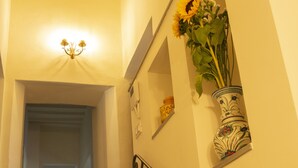 Een trap met een leuning, een wandplank met een bloevas, en een verlichte wandlamp.