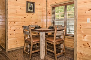 Un intérieur en bois avec une table et des chaises, une fenêtre avec des stores et un tableau au mur.