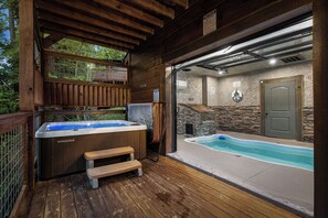 A wooden deck with a hot tub and a stone-walled indoor pool area.
