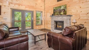 A log cabin interior with a stone fireplace, leather sofas, and large windows. - Free Attractions Pvt Pool, Mtn and City views. View fireworks from Hot tub! (Gatlinburg)