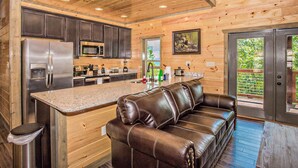 A modern kitchen with a built-in refrigerator, microwave, and stove. There is a leather sofa and a dining table in the living area. - Free Attractions Pvt Pool, Mtn and City views. View fireworks from Hot tub! (Gatlinburg)