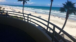 Une vue sur la plage depuis un balcon agrémenté de palmiers et doté d’une balustrade.