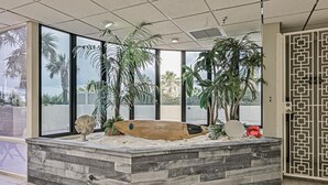 Un espace d’accueil avec un comptoir en bois, des palmiers et une planche de surf.