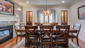 A dining room with a large wooden table, six chairs, a chandelier, and a fireplace. - Character Stay across Swan Lake Nature Sanctuary (Victoria)