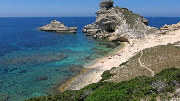 Un paisaje costero con formaciones rocosas, aguas azul turquesa y una playa de arena.