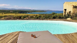 Una terraza de madera con piscina, un par de gafas de sol y vistas a un cuerpo de agua y montañas a lo lejos.