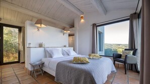 Un dormitorio con una cama grande, una mesita de noche, una silla y vistas al exterior.