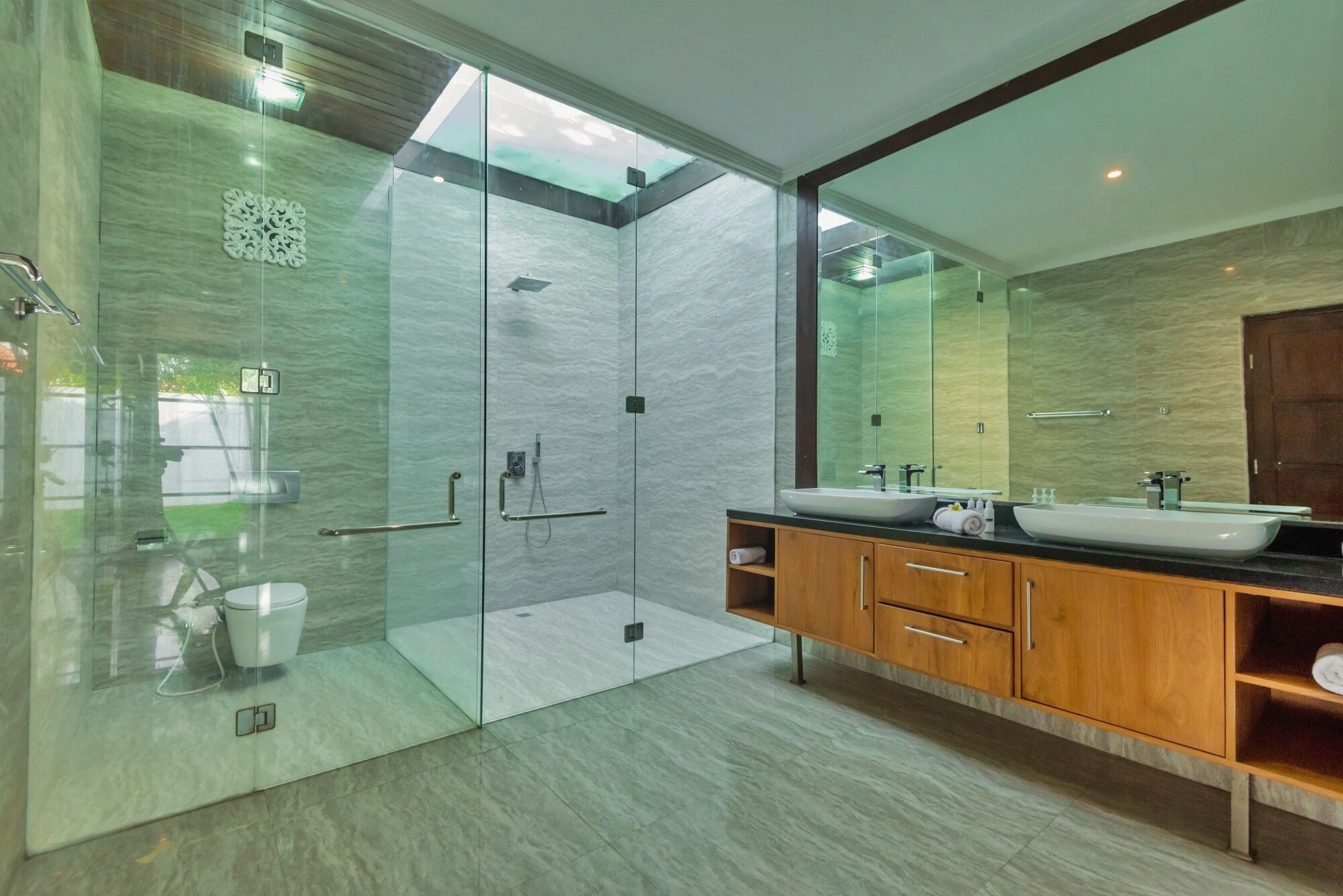 Une salle de bain moderne dotée d’une douche à parois de verre, d’un grand miroir et d’un meuble-lavabo en bois avec deux vasques.