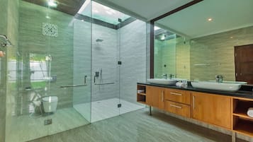 Une salle de bain moderne dotée d’une douche à parois de verre, d’un grand miroir et d’un meuble-lavabo en bois avec deux vasques.