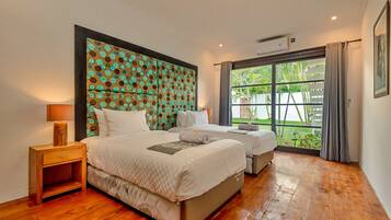 A hotel room with a large bed, a smaller bed, a nightstand, and a window with a view of greenery.