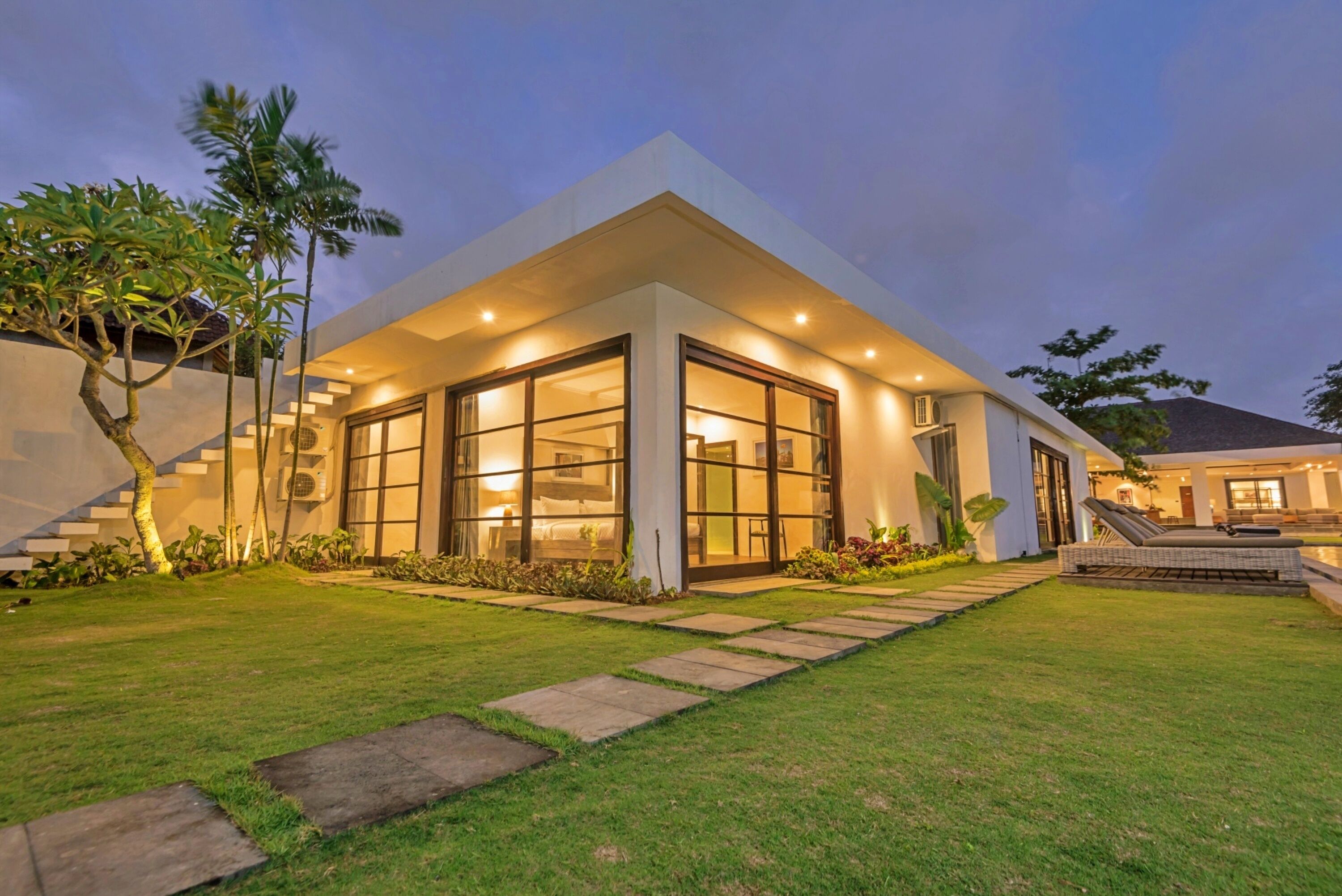 A modern house with large glass windows, a well-maintained lawn, and a staircase leading to the entrance.