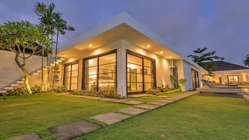A modern house with large glass windows, a well-maintained lawn, and a staircase leading to the entrance.