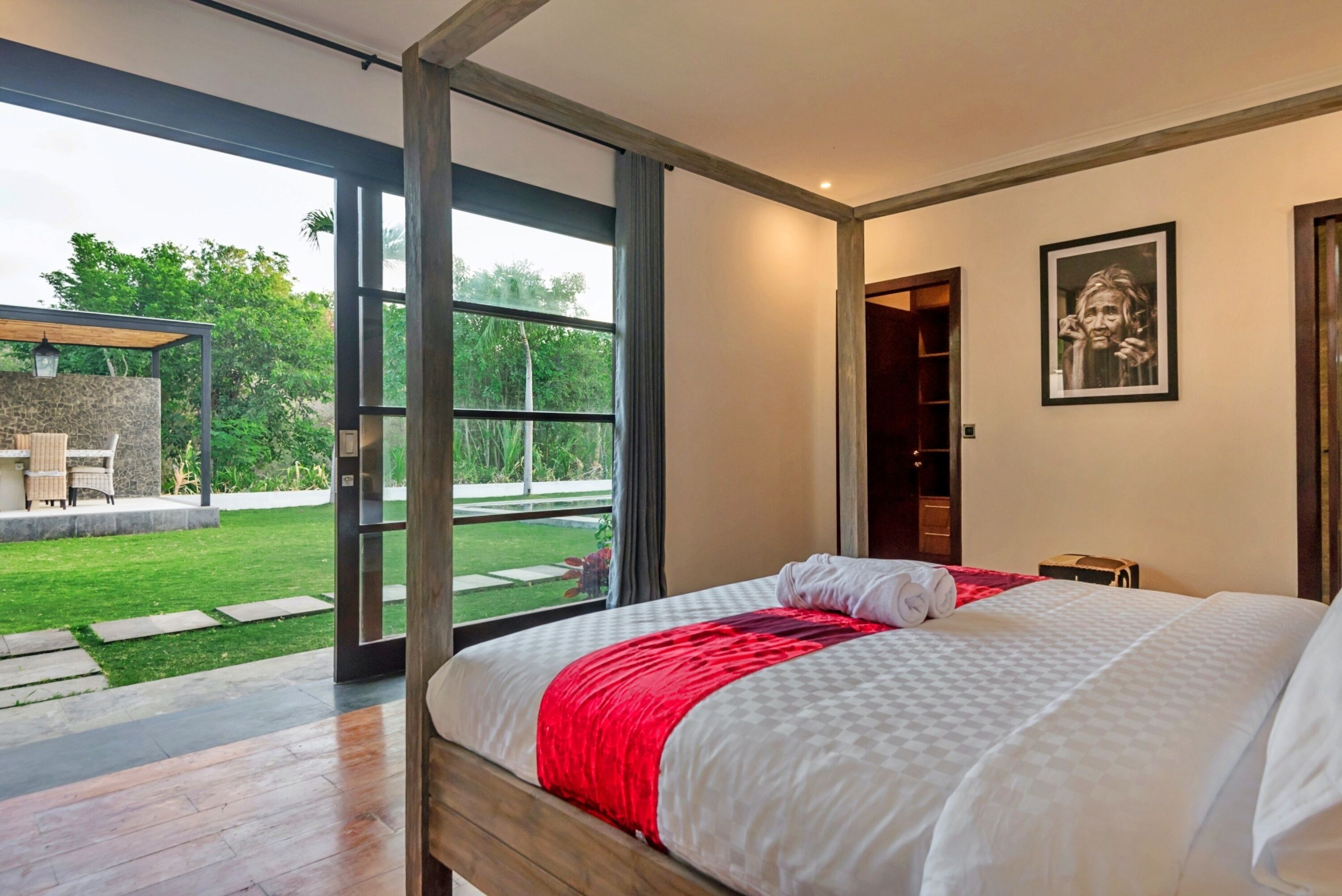 A bedroom with a large bed, a red throw, and a view of a garden through a glass door.