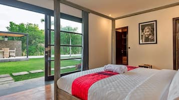 A bedroom with a large bed, a red throw, and a view of a garden through a glass door.