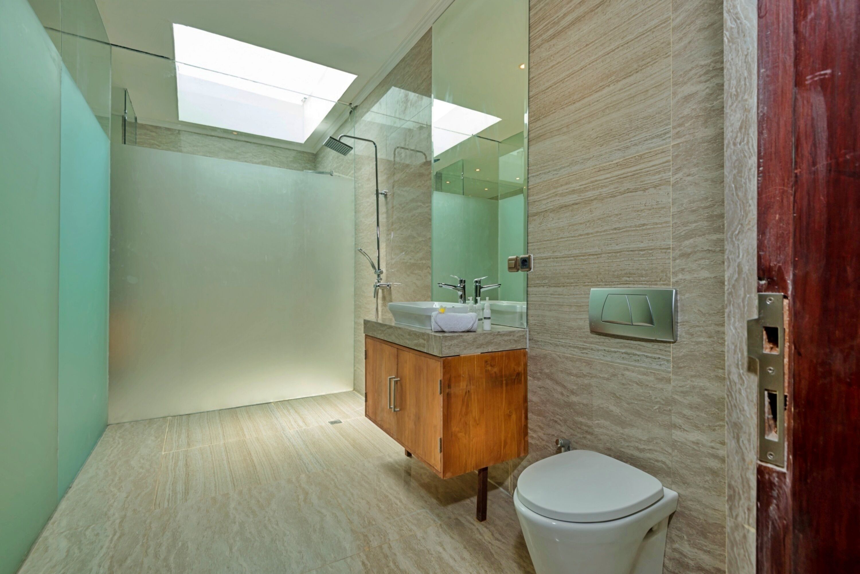 A modern bathroom with a skylight, a wooden vanity, a white toilet, and a large mirror.