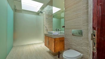 A modern bathroom with a skylight, a wooden vanity, a white toilet, and a large mirror.