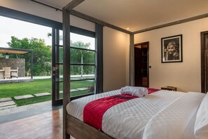 Une chambre dotée d’un grand lit, offrant une vue sur le jardin grâce à de grandes portes vitrées, et dont le plafond est constitué d’une structure en bois.