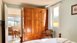 Un dormitorio con un armario de madera grande, una cama con ropa blanca, una silla y una ventana.