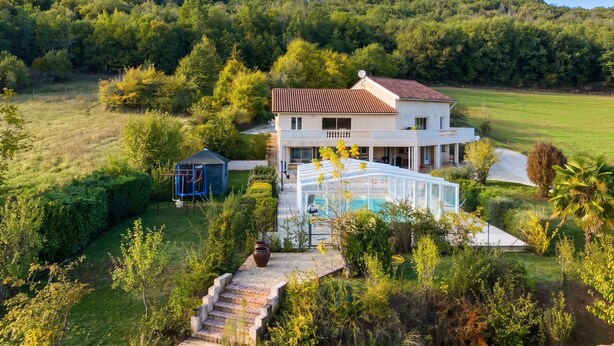 Una casa de dos pisos con piscina, rodeada de un paisaje verde exuberante y una colina al fondo.