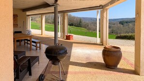 Un patio al aire libre con una parrilla, asientos y vistas al campo.