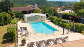 Una piscina con sillas de descanso, una estructura de vidrio y vistas a un paisaje montañoso.